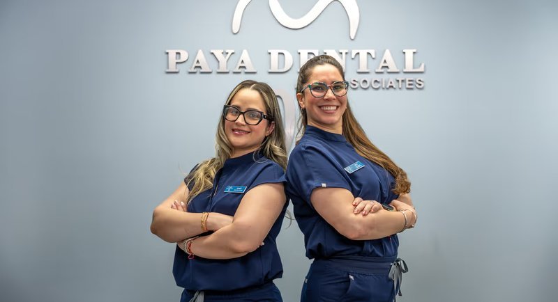 Two Paya Dental team members in front of the office logo